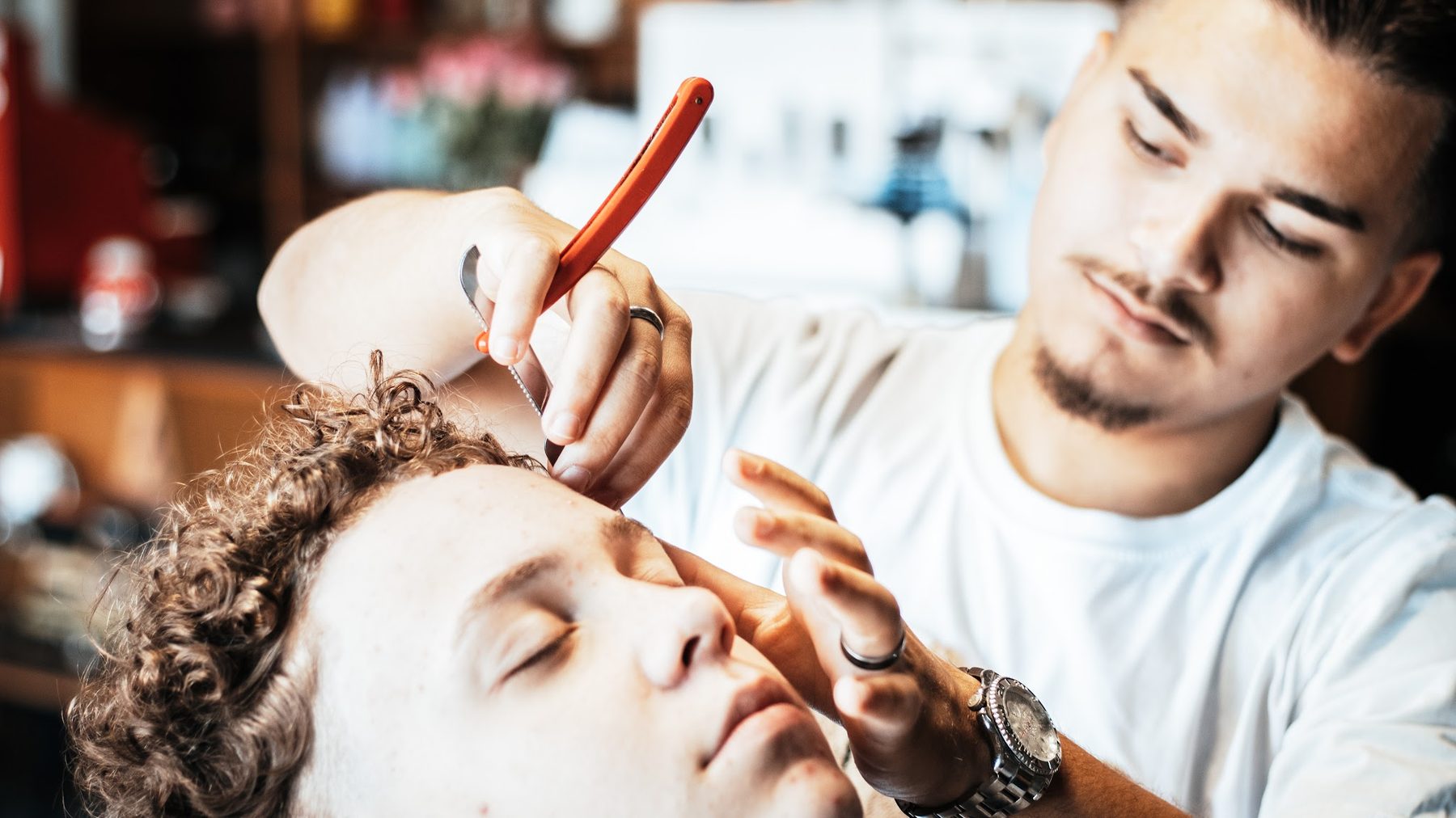 Een barber van Coupe 66 zet met een scheermes de contouren strak bij een klant met krullen