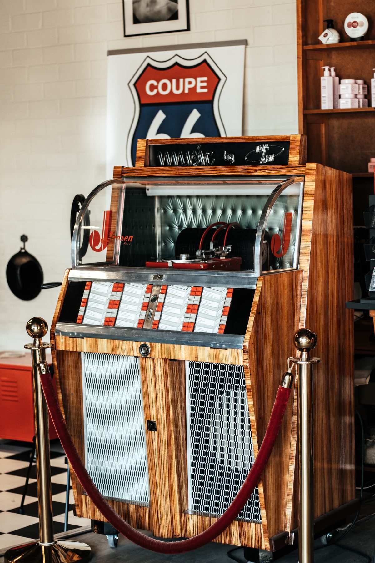 De jukebox van Coupe 66 onder het COUPE 66-bord, met een rood koord en zwart-witte tegels